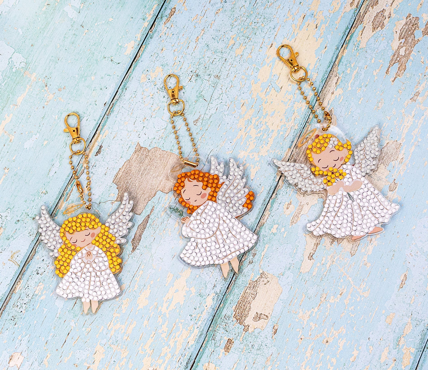 Three angel keychains on a textured blue surface