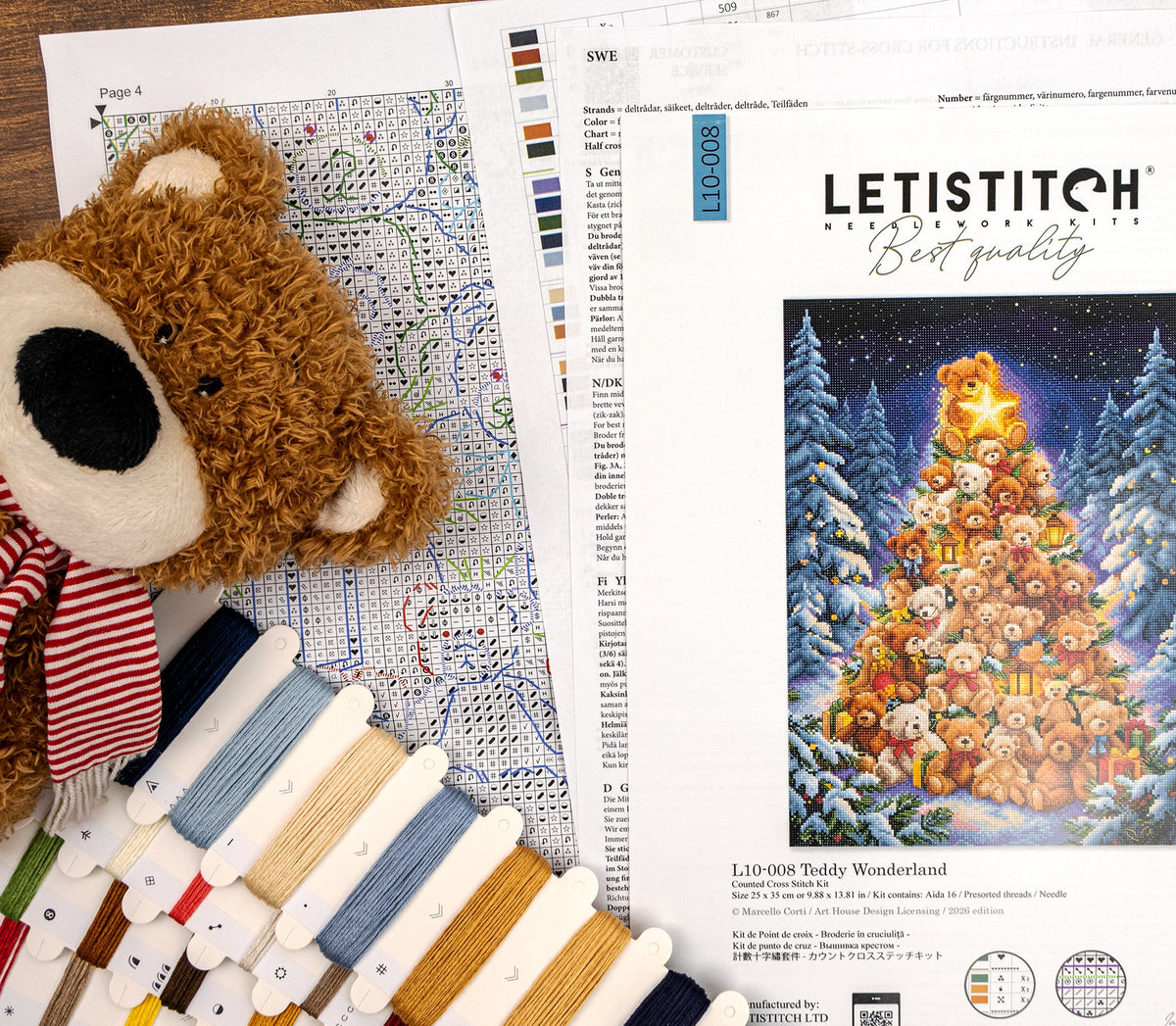 Letistitch Needlework 'Teddy Wonderland' embroidery kit pages and materials arranged on a wooden surface, including a teddy bear plush, color swatches, thread cones, and an embroidery pattern sheet showing a decorated Christmas tree made of teddy bears.