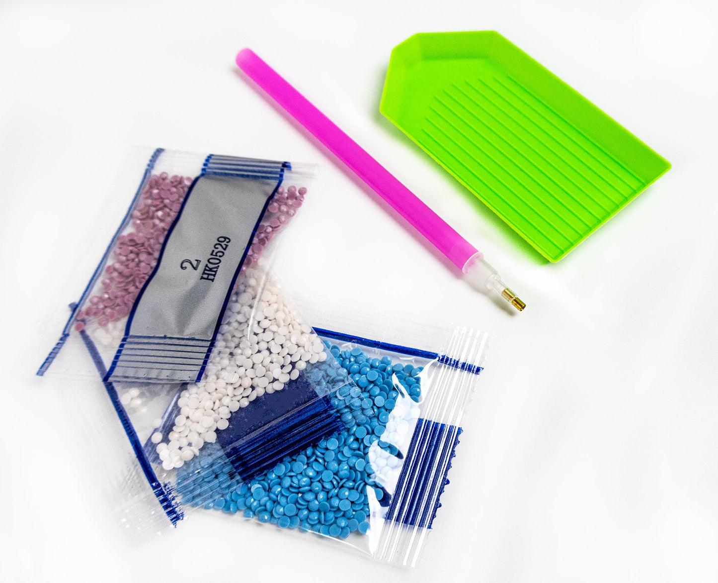 Packaged crystals with a pink tool and green plastic component on a white background