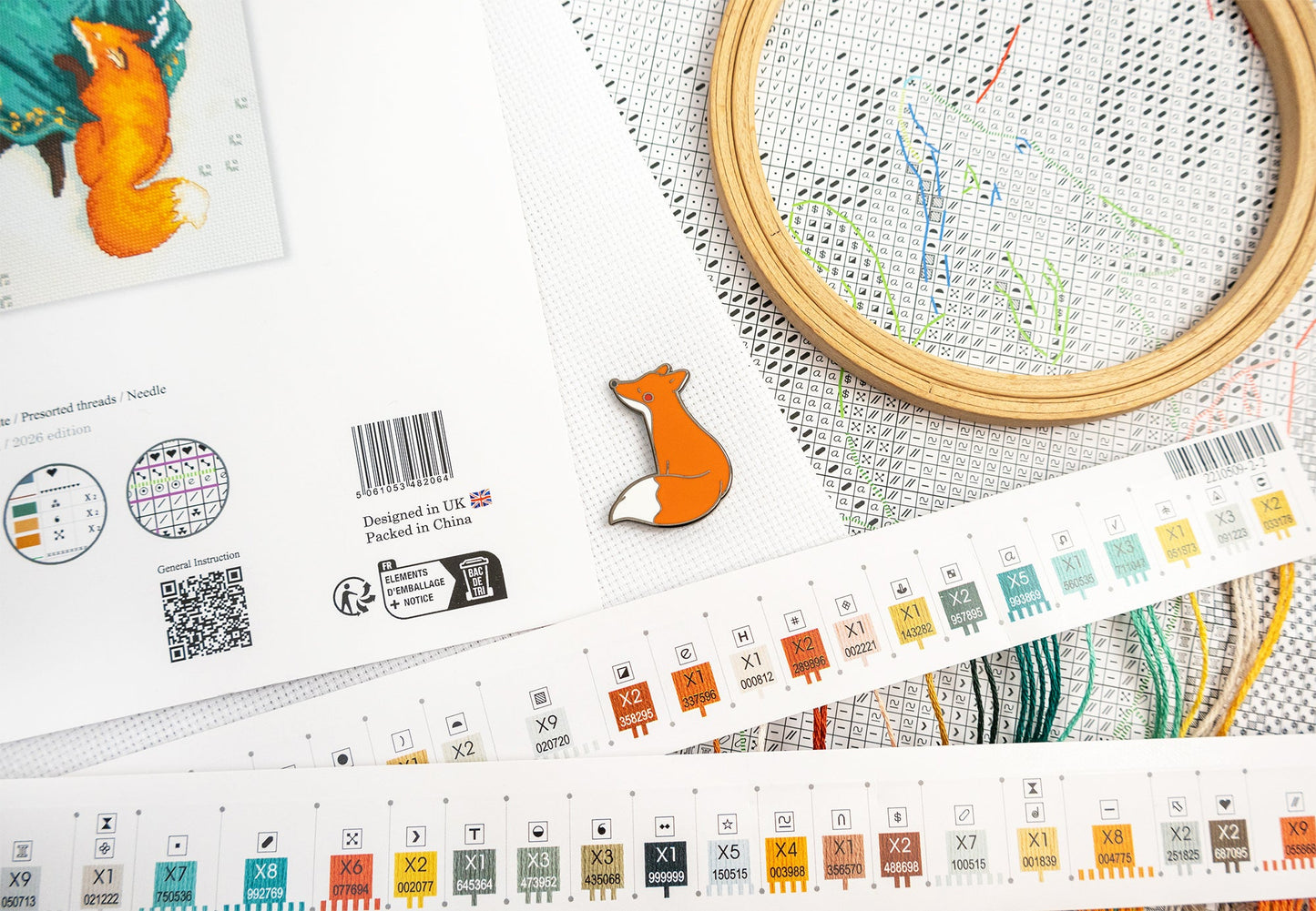 Embroidery kit with pattern chart, wooden hoop, and fox-themed design on a white surface.