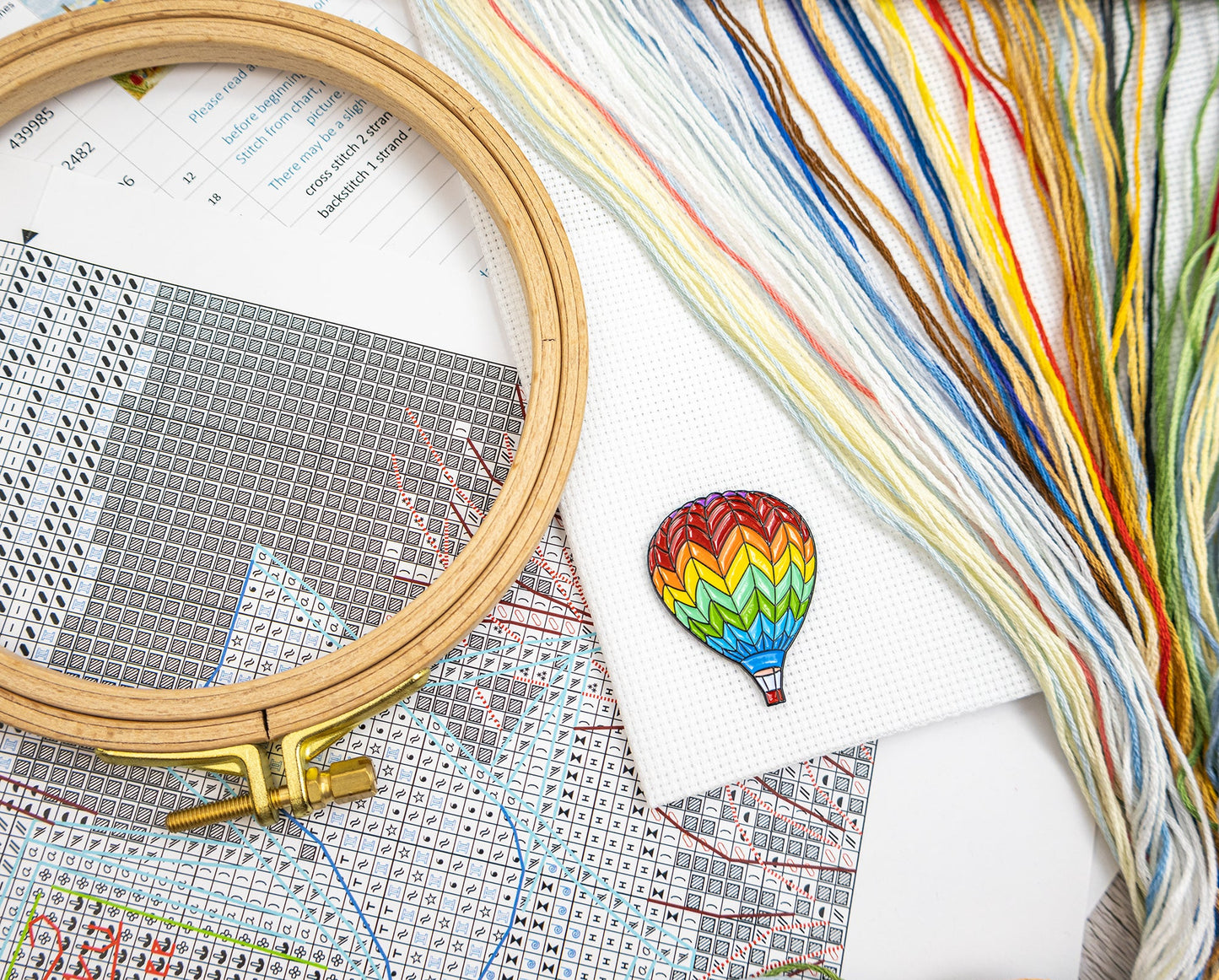 Embroidery hoop and colorful thread with a cross-stitched hot air balloon on a patterned paper background
