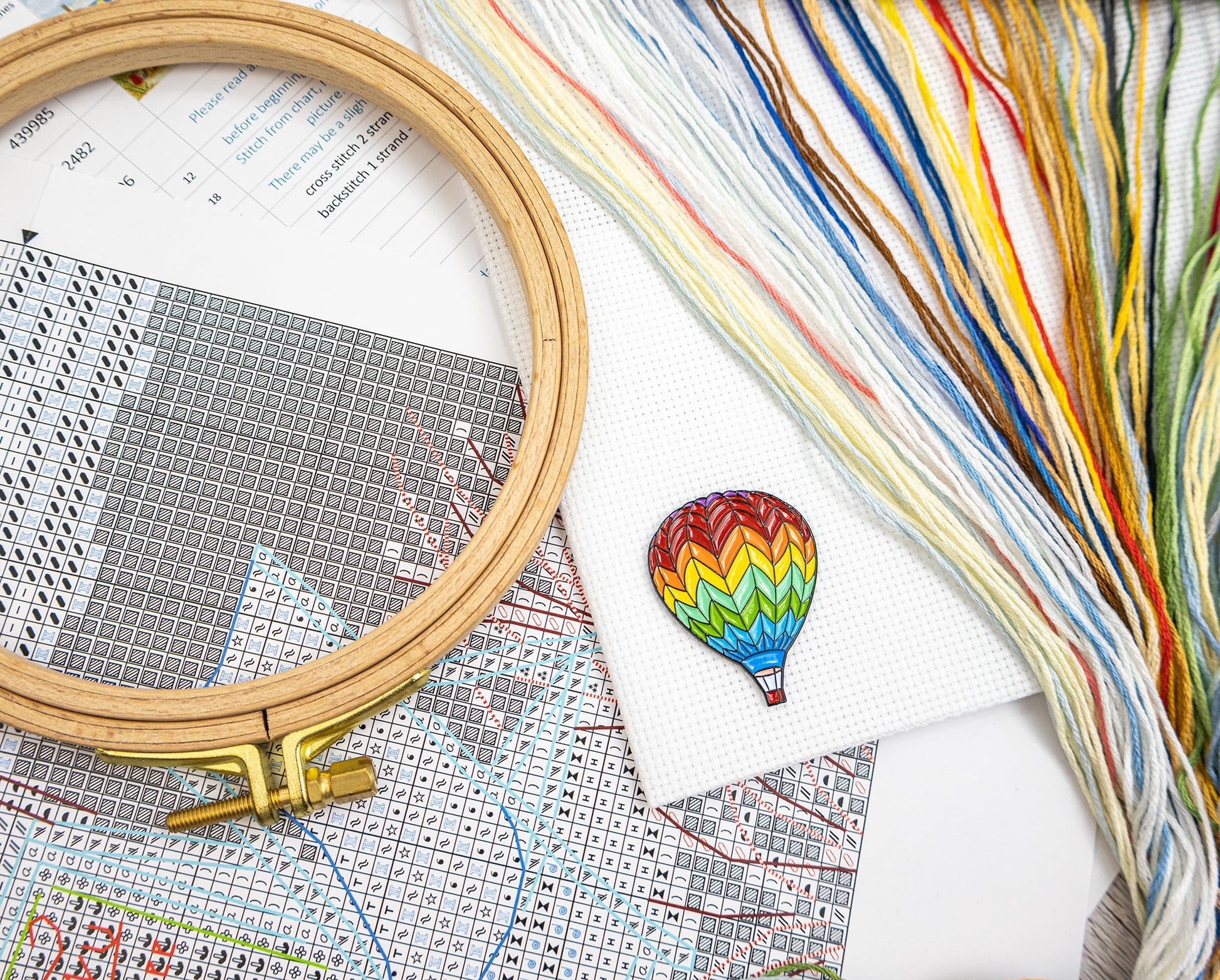 Embroidery hoop and colorful thread with a cross-stitched hot air balloon on a patterned paper background