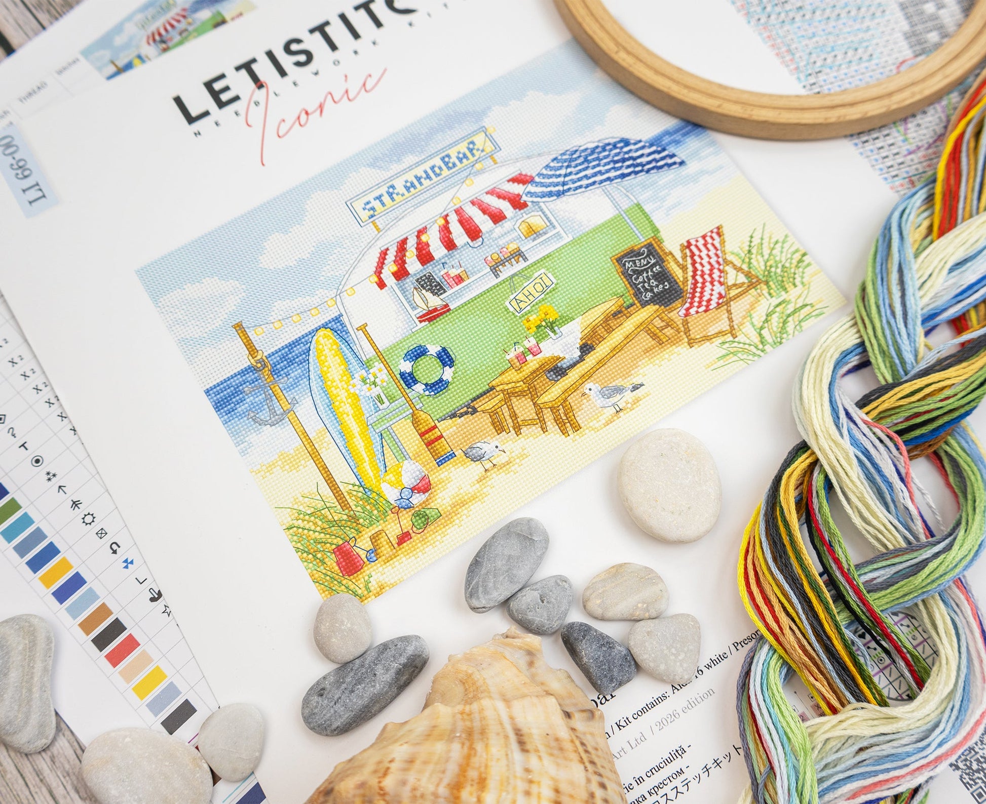 Color swatch book with a beach scene illustration, yarn skeins, stones, and shells on a textured surface.