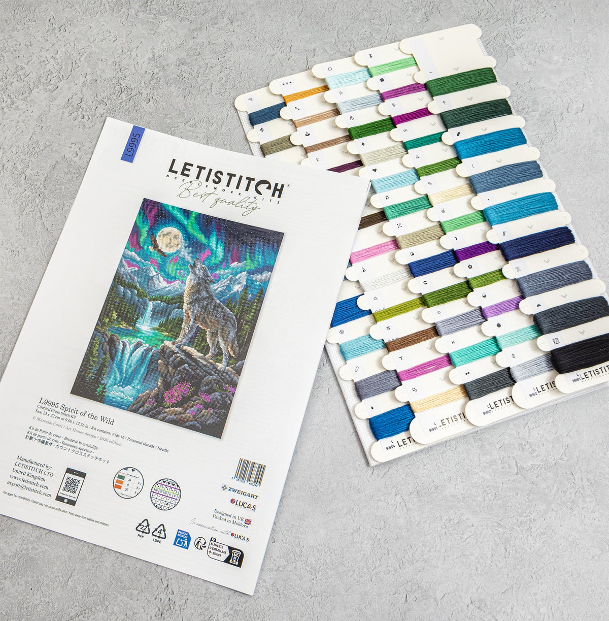 Letistitch embroidery floss set with a printed sample card showing a wolf and aurora design, alongside a large array of colorful thread spools on a light gray textured background.