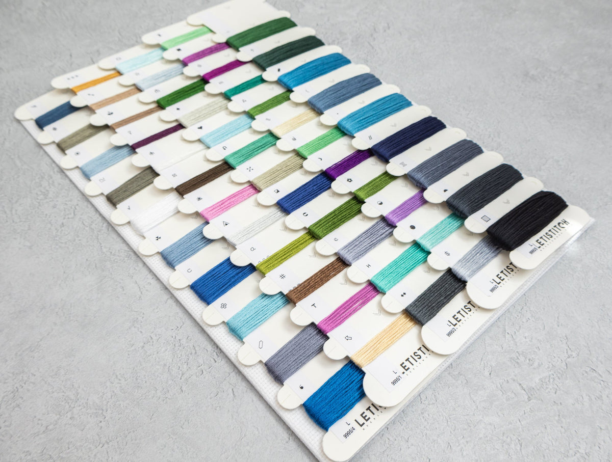 A white display board filled with many small thread spools in assorted colors, photographed on a light gray textured surface.