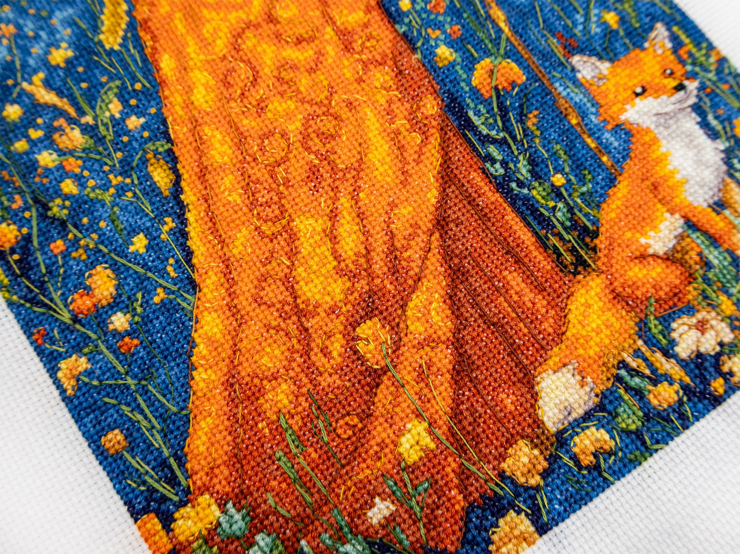 Embroidery of a fox in a natural setting with flowers and blue background