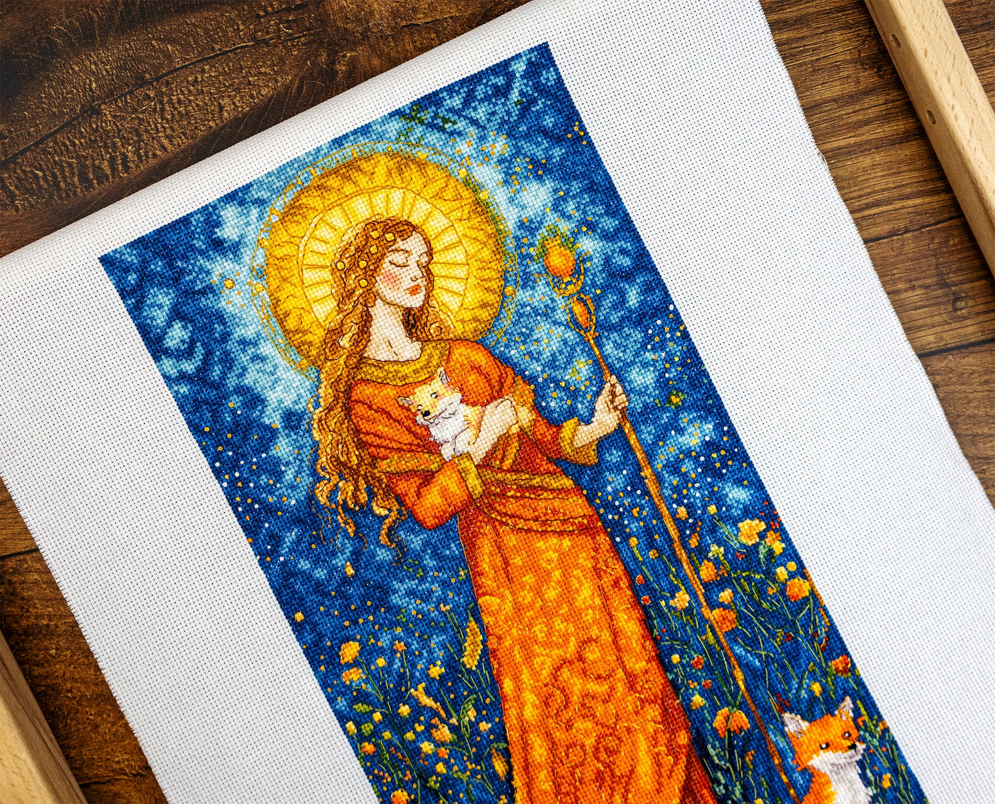 Embroidery of a woman holding a fox against a starry night sky with flowers.