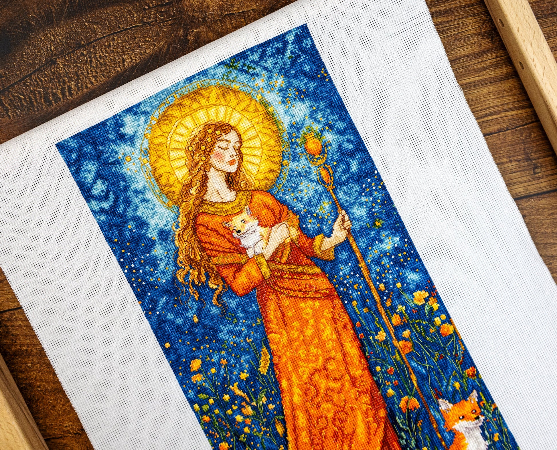 Embroidery of a woman holding a fox against a starry night sky with flowers.