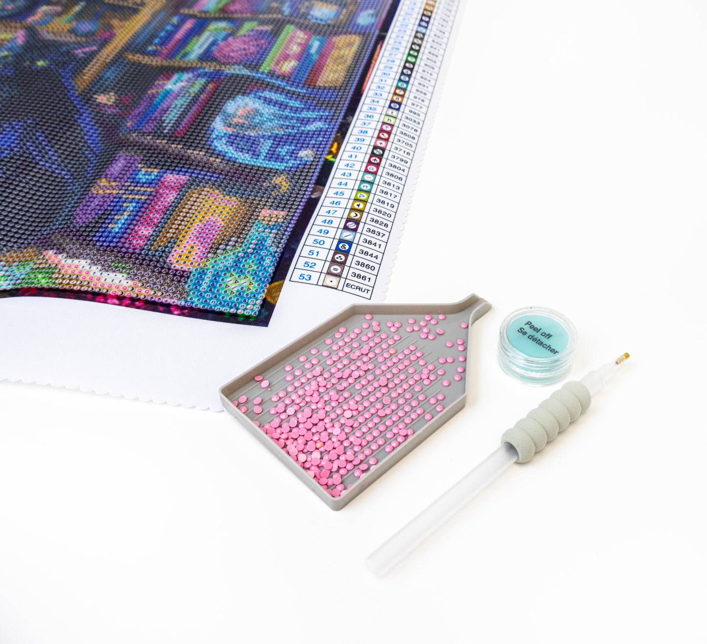 Diamond painting kit with a partially completed artwork, pink beads, a tool, and a color chart on a white surface.